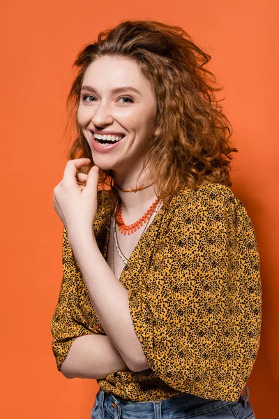 stock image Portrait of young red haired woman in blouse with abstract print and jeans laughing and looking at camera on orange background, stylish casual outfit and summer vibes concept, Youth Culture