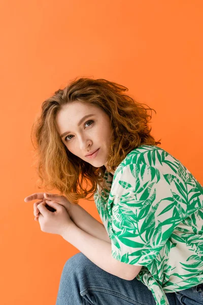 stock image Portrait of stylish and confident redhead model in blouse with floral pattern and jeans looking at camera isolated on orange, trendy casual summer outfit concept, Youth Culture