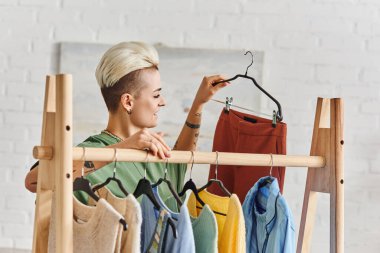 Genç ve dövmeli kadın, moda saç stili askısı, moda pantolonları, modern oturma odasında günlük kıyafetler, sürdürülebilir moda ve dikkatli tüketim konsepti.