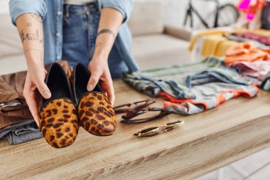 exchange market, cropped view of tattooed woman with trendy animal print shoes near sunglasses and clothes on table at home, sustainable living and mindful consumerism concept clipart