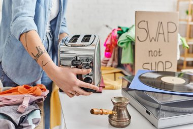 Genç ve dövmeli bir kadının vinil kayıt cihazının yanında elektrikli tost makinası tutması, takas sırasında çakmak ve ikinci el giysiler giymesi alışveriş değil, sürdürülebilir yaşam ve dairesel ekonomi konsepti