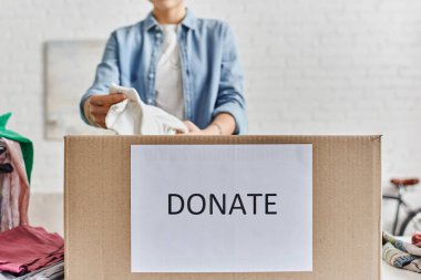 Sosyal iyi girişimler, kısmi bakış açısı evde bağış mektupları olan karton kutuda kıyafet paketleyen genç kadın, bulanık geçmiş, sürdürülebilir yaşam ve sosyal sorumluluk kavramı