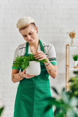 bitki bakımı, bahçe işleri, yeşil önlüklü gülen kadın modern oturma odasında ayakta dururken doğal saksı bitkisine dokunuyor sürdürülebilir ev dekorasyonu ve yeşil yaşam konsepti