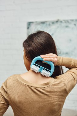 Kahverengi kazaklı esmer kadının evdeki bulanık oturma odasında kendine bakım ritüeli sırasında masaj yaparken sırt masajı yapması bütünsel sağIık ve sağlık konsepti, gerginlik giderme.