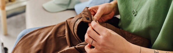 cropped view of young and tattooed woman checking button on leather pants during clothes decluttering at home, sustainable living and mindful consumerism concept, banner