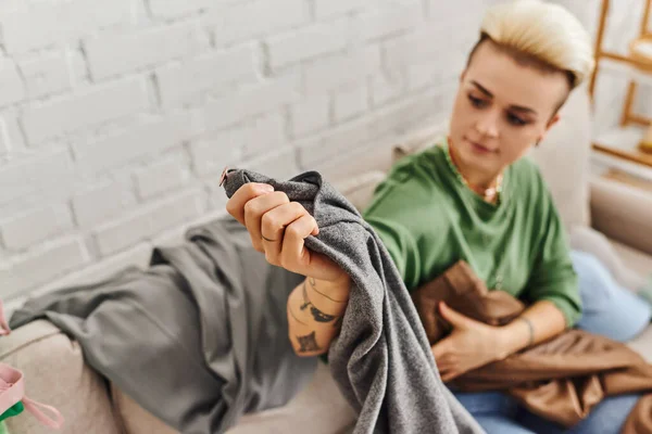Jovem Mulher Tatuada Sentada Sofá Sala Estar Segurando Calças Cinza — Fotografia de Stock