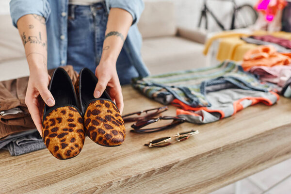 exchange market, cropped view of tattooed woman with trendy animal print shoes near sunglasses and clothes on table at home, sustainable living and mindful consumerism concept