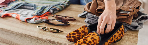 partial view of woman placing fashionable animal print shoes near sunglasses and pre-loved clothes on table at home, eco-friendly swaps, sustainable living and mindful consumerism concept, banner