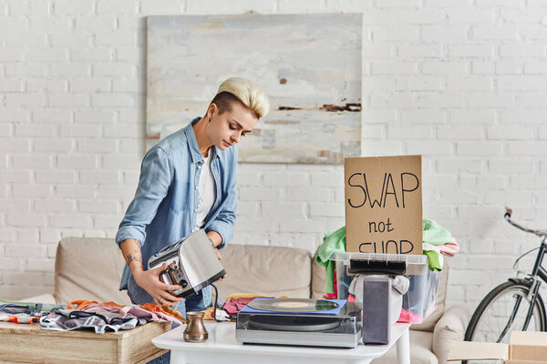 eco-friendly swaps, collaborative consumption, tattooed woman with electric toaster near vinyl record player, cezve, plastic container with clothes, sustainable living and circular economy concept