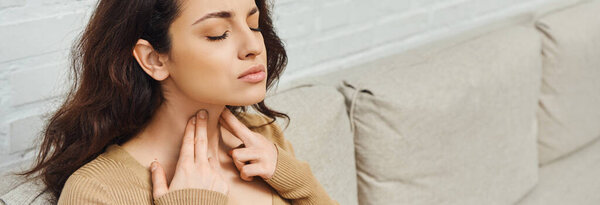 Young woman in casual jumper massaging lymphatic nodes on neck during wellness routine on couch at home, self-care ritual and holistic wellness practices concept, banner, tension relief