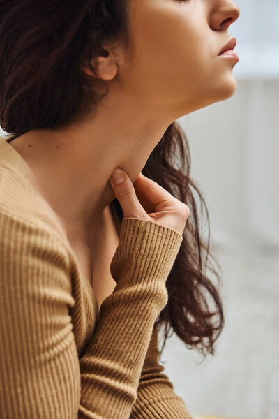 Cropped view of brunette young woman in brown jumper massaging Tyrode on neck during self-massage routine at home, self-care ritual and holistic healing concept, balancing energy