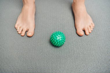 manual massage ball on fitness mat near feet of woman at home, body relaxation and holistic wellness practices, balancing energy concept, top view, barefoot 