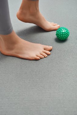 Çıplak ayaklı bir kadının evdeki el masajı topunun yanında duran halinin görüntüsü, vücut gevşemesi ve bütünsel sağlık uygulamaları, enerji dengelemesi.