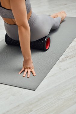 Spor giyimli genç bir kadının evdeki doğal sağlık uygulamaları sırasında modern masajcı ve fitness minderine oturması sağlıklı lenf sistemi konseptini ve miyofasiyal salınımını sürdürmesi.