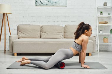 Çıplak ayaklı, esmer, spor kıyafetleriyle masaj yapan, modern tekerlekli bacakları olan, spor ayakkabılı, spor ayakkabılı, sağlıklı lenfatik sistem kavramını koruyan, miyofasiyal salınımını sürdüren genç bir kadının yan görüntüsü.