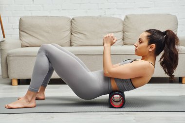 Spor kıyafetleri içinde genç ve çıplak ayaklı bir kadının arka koltukta masaj yapması evde spor paspası takması, sakinlik hissi ve rahatlama kavramı, miyofasiyal rahatlama.