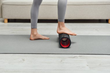 Çıplak ayaklı genç bir kadının spor kıyafetleri içinde ayak masajı yapması ve evdeki spor minderinin üzerinde durması lenf akışını ve evdeki gerginliği arttırıyor.