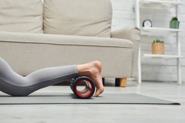 Aktif giyimli çıplak ayaklı bir kadının masajcı bacaklarıyla spor salondaki oturma odasındaki kanepenin yanındaki masaj minderinde lenf akışını ve ev konseptindeki sağlığını yükseltirken görüntüsü, gerilim giderici.