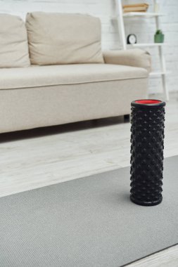 Evdeki oturma odasındaki bulanık kanepenin yanında duran modern siyah tekerlekli masaj aleti, ev konseptinde lenf akışını ve sağlığını teşvik ediyor.