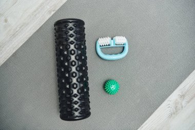 Top view of roller and handle massagers and massage ball lying on fitness mat on floor at home, natural health practices and home-based massage concept, health and relaxation, wellness routine  clipart