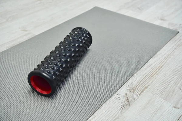 stock image Modern black roller massager lying on fitness mat on floor at home, promoting lymph flow and wellness at home concept, beauty and wellness routine, health and relaxation 