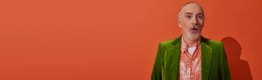 trendy senior man with shocked face expression looking at camera on red orange background, grey hair and beard, green velour blazer, fashion and age concept, banner with copy space clipart