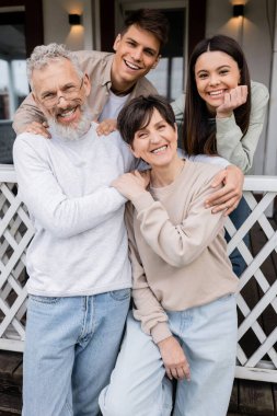 Aile fotoğrafı, mutlu ebeveynler günü, neşeli orta yaşlı ebeveynler aile evinin verandasında kızlarına ve küçük oğluna sarılıyorlar, kutlama, bağ kurma, hatırlanacak anlar, modern ebeveynlik, June. 