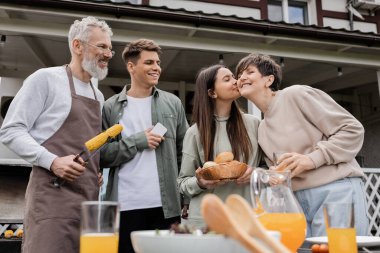 Ebeveynler günü, mutlu orta yaşlı ebeveynler, aile yemeği partisi, annesinin yanağını öpen genç kız, kardeşler, ızgara mısırlı maşa tutan baba, yazlık ev, banliyö hayatı. 