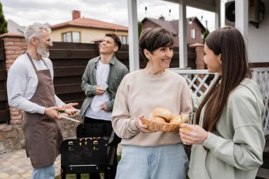 Ebeveynler gününü kutluyoruz, orta yaşlı anneler çörek tutuyor ve genç kız, baba ve oğulla konuşuyor barbekü ızgarasında yemek hazırlıyorlar, kahkaha, modern ebeveynlik, banliyö hayatı, yaz mevsimi