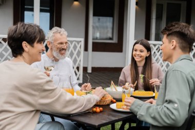 Aile bbq partisi, ebeveynler günü kutlaması, yetişkin kardeşinin yanında oturan neşeli ergen kız, yazlık evin arka bahçesinde oturup, birlikte vakit geçirip ızgara bbq yemeği yiyen kız. 