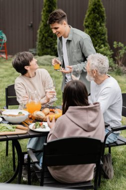 Mutlu genç bir adam portakal suyu tutuyor ve ailesinin yanında orta yaşlı bir anneyle konuşuyor. Ve arka bahçede aileler günü kutlaması sırasında, aile bağları kavramını sevgiyle anan...