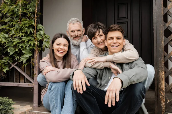 Positive Middle Aged Parents Hugging Children Looking Camera While Sitting — Stock Photo, Image