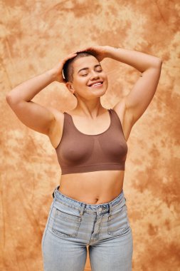 body acceptance, curvy and cheerful woman in crop top posing on mottled beige background, smiling with closed eyes, representation of body, different shapes, generation z, youth, tattooed   clipart