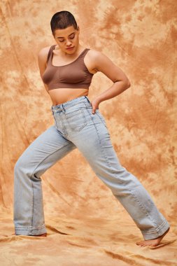 denim fashion, generation z, young curvy woman with tattoos posing with hand in pocket on mottled beige background, different shapes, body positivity movement, self-esteem, confidence, short haired  clipart