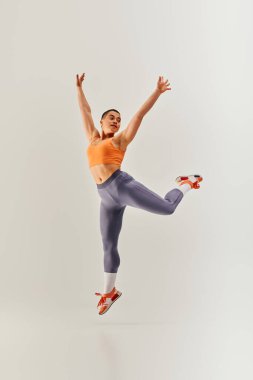 Vücut pozitifliği hareketi, genç kıvrımlı ve kısa saçlı kadın gri arka planda atlama, kadın fitness, güçlendirme, motivasyon, spor kıyafeti, güç ve sağlık, vücut imajı 