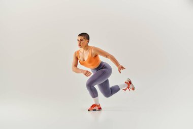 Dayanıklılık, vücut pozitifliği, kısa saçlı ve kıvrımlı kadın gri arka plan üzerinde çalışıyor, kadın fitness, motivasyon, eğitim, spor giyim, güç ve sağlık. 