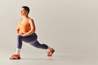 body positivity movement, young short haired woman doing lunges on grey background, curvy fitness model in sportswear, empowerment, motivation, working out, strength and health  clipart
