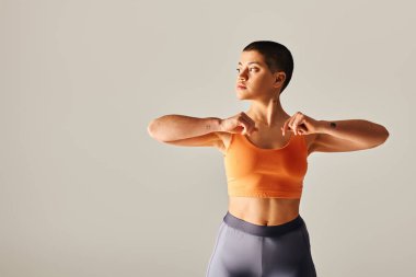 Vücut çeşitliliği, dövmeli ve kısa saçlı kadın gri arka plan, spor giyim, güçlendirme, motivasyon, güç ve sağlık alanlarında kıvrımlı fitness modeli üzerinde çalışıyor. 