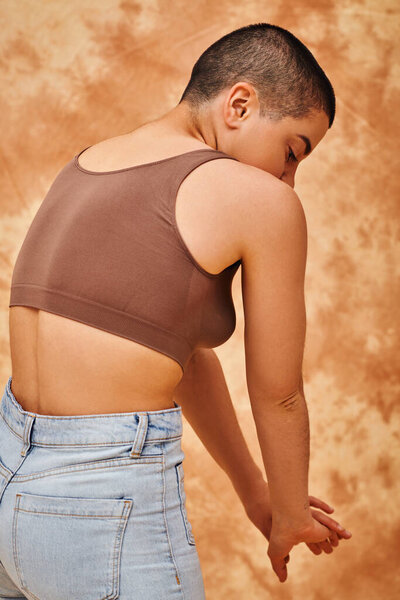 body diversity, denim fashion, curvy and tattooed woman in jeans and crop top standing on mottled beige background, casual attire denim fashion,  self-acceptance, generation z, body love