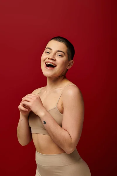 Αυτοαποδοχή Κατάπληκτος Και Τατουάζ Γυναίκα Μπεζ Εσώρουχα Ποζάρουν Κόκκινο Φόντο — Φωτογραφία Αρχείου