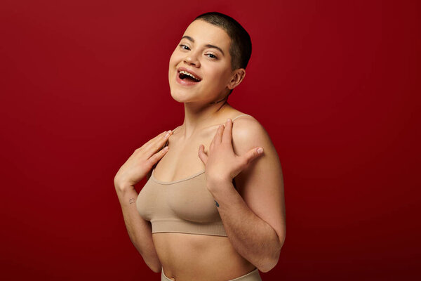 self acceptance, excited and tattooed woman in beige underwear posing on red background, body positivity, curvy fashion, comfortable in skin, self-acceptance, generation z, body diversity, laughter 