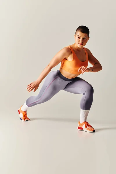 身体积极 年轻的短发女子在灰色背景下做突然运动 在运动服 力量和健康方面的曲线健身模型 — 图库照片