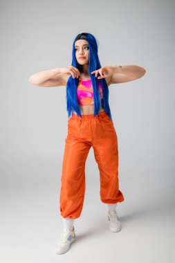 Moda trendleri, mavi saçlı, gri arka planda renkli pozlar veren genç bir kadın, tam boy, funky görünüm, bireysellik, modern tarz, kentsel moda, canlı renk, model. 