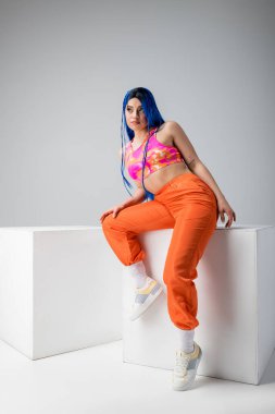 urban fashion, tattooed woman with blue hair posing in colorful clothes near white cubes on grey background, full length, individualism, modern style, vibrant color, young model  clipart