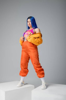 Tam boy, moda ileri, gri arka planda mavi saçlı genç kadın, beyaz küplerin üzerinde duruyor, canlı renk, kadın model, bireysellik, şehir modası 