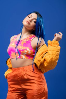 colorful clothes, dyed hair, female model with blue hair posing in puffer jacket on blue background, hand in pocket, vibrant color, urban fashion, individualism, young woman with funky look  clipart