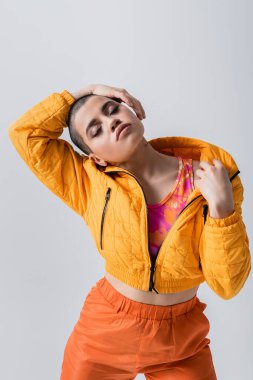 outerwear, individualism, fashion model posing with closed eyes, young woman with short hair standing in yellow puffer jacket on grey background, isolated, youth culture, casual wear clipart
