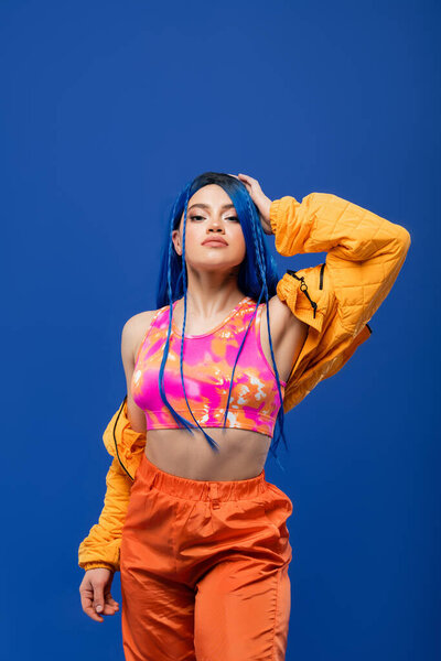 vibrant look, dyed hair, female model with blue hair posing in puffer jacket on blue background, vibrant color, urban fashion, individualism, young woman with funky style