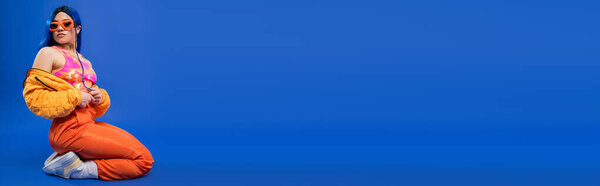 заявление о моде, полная длина женской модели с синими волосами и триумфальными солнцезащитными очками, сидящими на синем фоне, бунтарский стиль, современная мода, триумфальный аксессуар, молодость, молодая красивая женщина, баннер