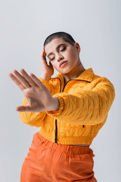 outerwear, casual attire, fashion model posing with outstretched hand, young woman with short hair and closed eyes in yellow puffer jacket on grey background, isolated, youth culture 
